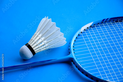 Badminton racket and badminton feather shuttlecock on blue floor of indoor badminton court, soft and selective focus, concept for playing badminton in daily life to get strong health and good feeling. © Sophon_Nawit