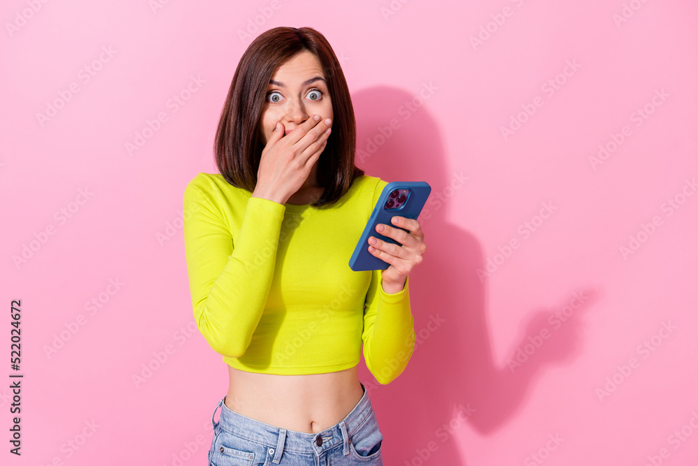 Photo of pretty shocked lady wear yellow top arm cover lips reading modern gadget empty space isolated pink color background Photo of pretty shocked lady wear yellow top arm cover lips reading modern gadget empty space isolated pink color background