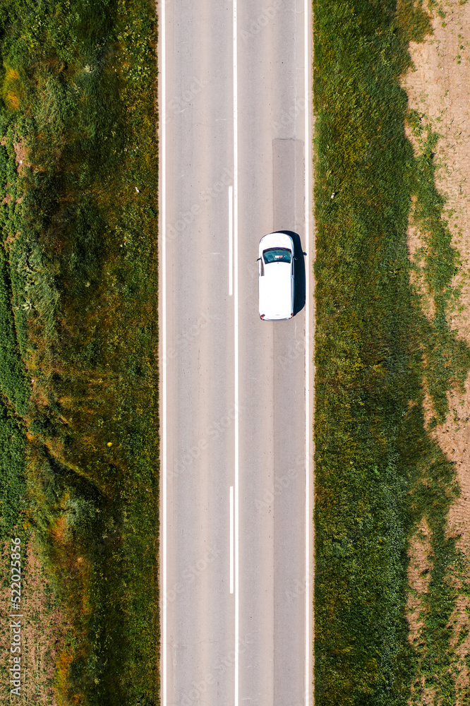 White multi-purpose vehicle is driving along the road through countryside landscape on hot summer afternoon, drone pov White multi-purpose vehicle is driving along the road through countryside landscape on hot summer afternoon, drone pov