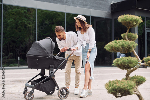 Looking at the kid. Young parents having a walk with baby carriage outdoors