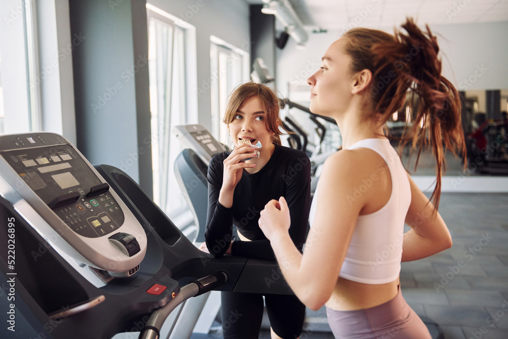 Running on the racetrack. Two women in sportive clothes have fitness day in the gym together Running on the racetrack. Two women in sportive clothes have fitness day in the gym together