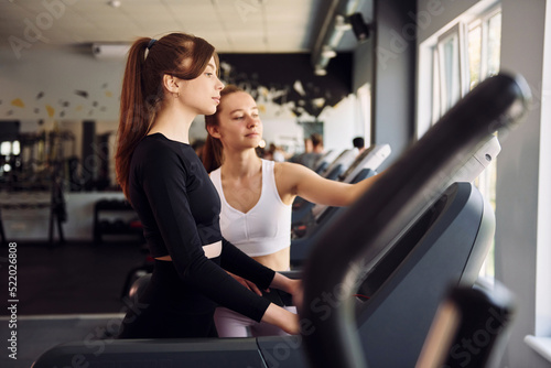 Showing how to use racetrack. Two women in sportive clothes have fitness day in the gym together
