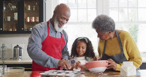 Video of happy african american granddaughter baking with grandparents in kitchen