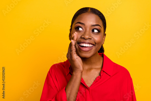 Photo of young cheerful girl arm near mouth curious look empty space say gossip isolated over yellow color background