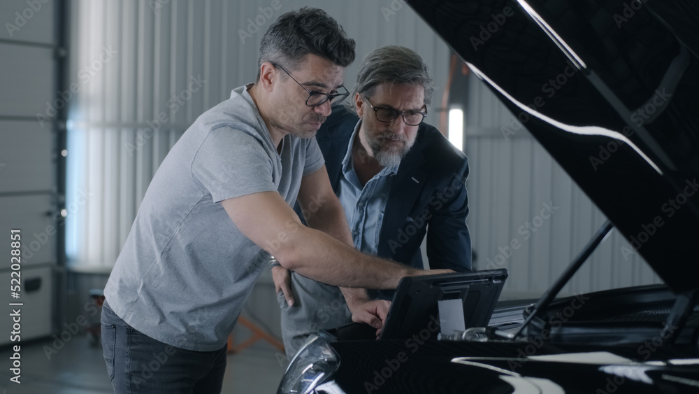 Man mechanic talking to client and checking car engine during diagnostics in car service using tablet computer Man mechanic talking to client and checking car engine during diagnostics in car service using tablet computer