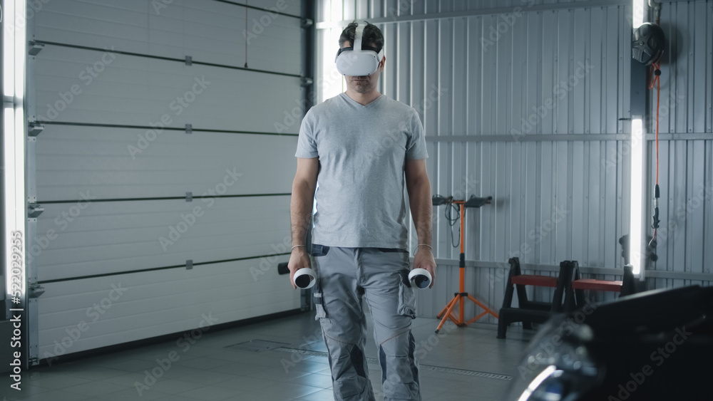 Man worker in uniform in a modern virtual reality glasses with controllers checking and testing a car after repairing in a car service Man worker in uniform in a modern virtual reality glasses with controllers checking and testing a car after repairing in a car service
