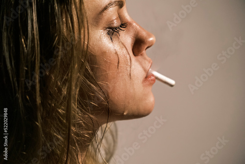 Crying young woman with cigarette in her mouth. Portrait of side view of unhappy woman experiencing an emotional crisis in her life. Domestic psychological and physical violence