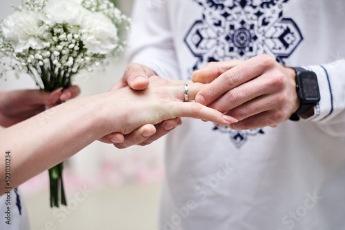 Close up picture of bride and groom s hands putting on a wedding ring at official marriage ceremony. Bride and groom are getting married at city hall. National ukrainian embroidered costumes