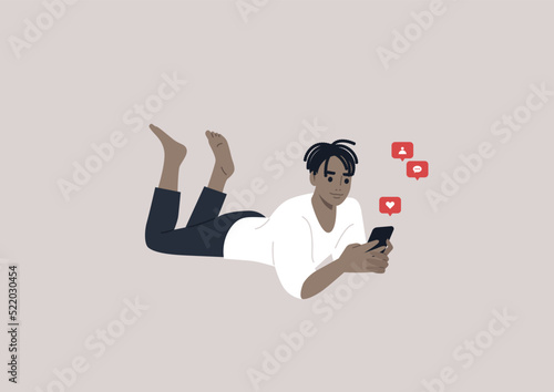 A young male African character lying on their stomach and checking their mobile phone notifications