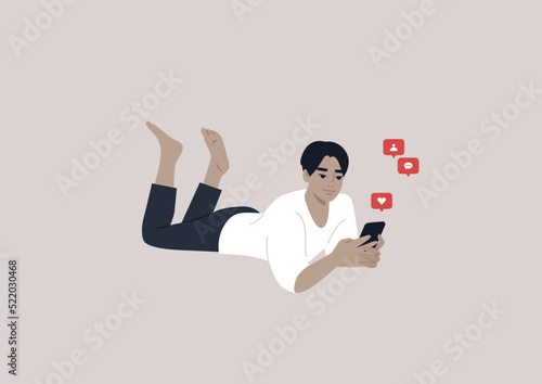 A young male Asian character lying on their stomach and checking their mobile phone notifications