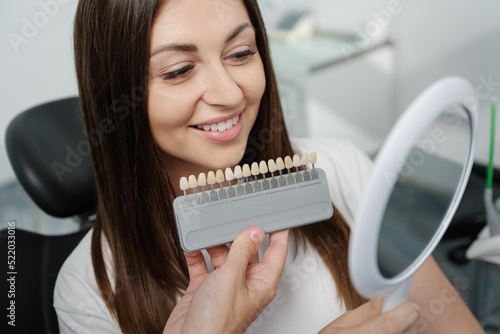 Young man dentist in white coat show veneers enamel color palette for beautiful patient woman