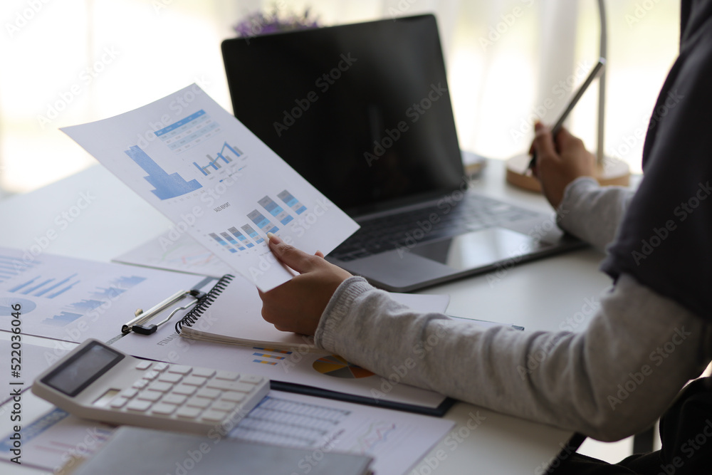 Attractive Muslim businesswoman working with laptop and analyzing financial statements on desk in office. Attractive Muslim businesswoman working with laptop and analyzing financial statements on desk in office.