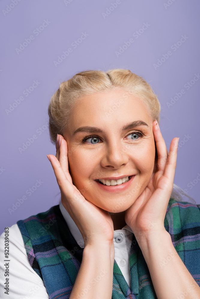 Portrait of smiling blonde student touching face isolated on purple Portrait of smiling blonde student touching face isolated on purple