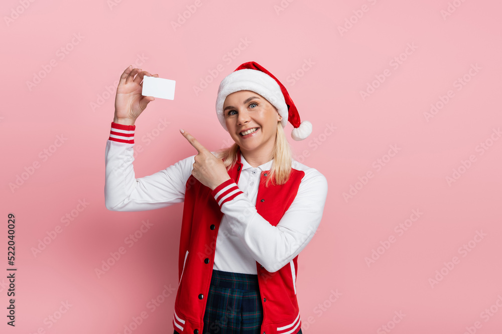 Cheerful woman in santa hat pointing at empty driving license on pink background