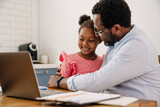 African american man hugging daughter while working on laptop at home