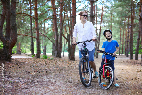 Cheerful mother and son riding a bicycle in forest