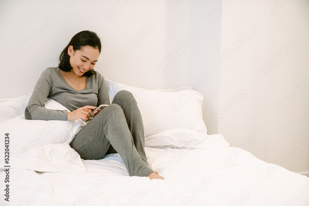 Young asian girl with phone sitting on the bed Young asian girl with phone sitting on the bed