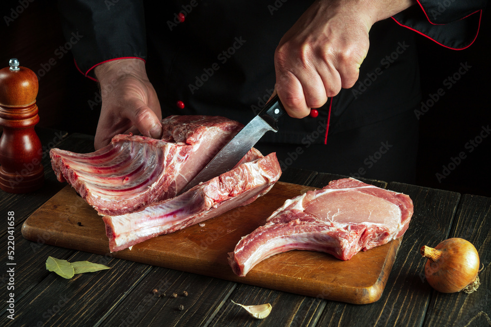 Slicing raw ribs with butcher or cook hands on kitchen cutting board. Barbecue grill. Idea for a restaurant or hotel menu on a dark background