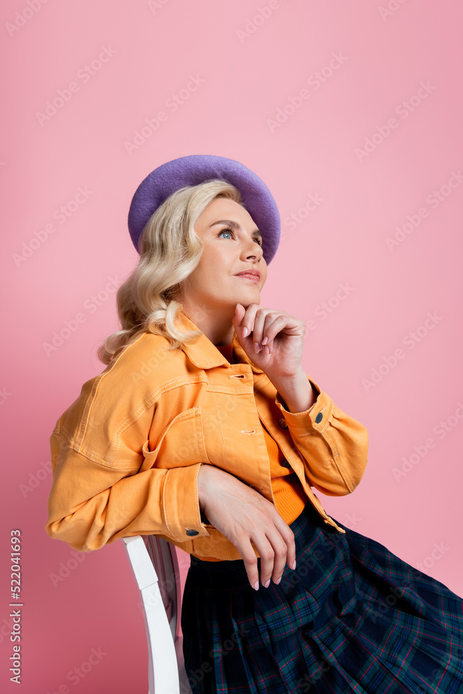 Dreamy woman in beret sitting on chair isolated on pink Dreamy woman in beret sitting on chair isolated on pink