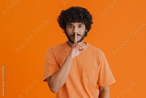 Young indian handsome curly man wearing t-shirt showing silence gesture