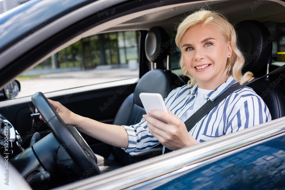 Blonde woman smiling at camera while sitting on driving seat in auto