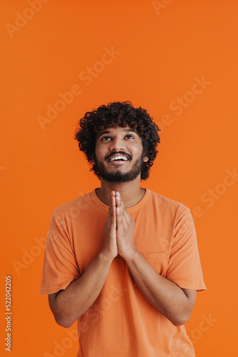 Young indian curly smiling man with folded hands looking upward © Drobot Dean