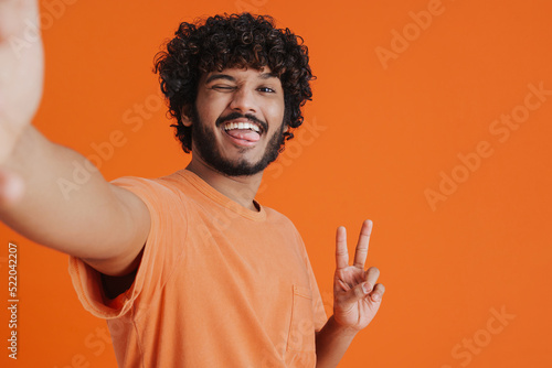 Selfie of young smiling handsome indian man in orange t-shirt