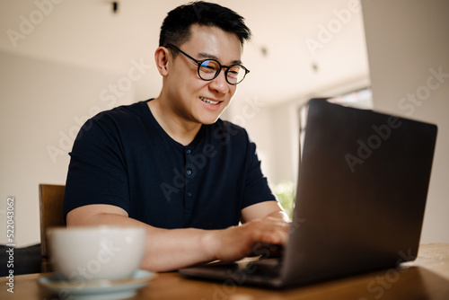 Adult smiling asian man in glasses studying with laptop