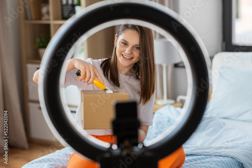 blogging, technology and people concept - happy smiling girl blogger with ring light and smartphone unpacking parcel box with knife at home © Syda Productions