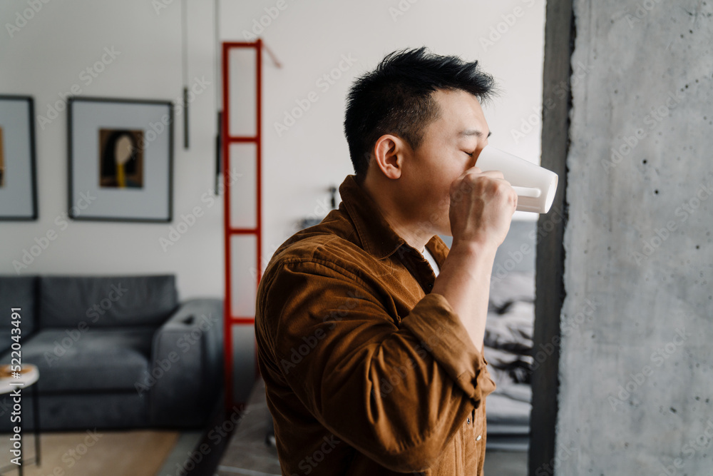 Brunette adult asian man drinking coffee from cup at home