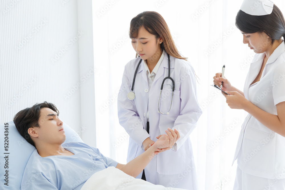 Female doctor and young male patient who lie on the bed while checking pulse, consult and explain with nurse taking note and supporting in hospital wards. Female doctor and young male patient who lie on the bed while checking pulse, consult and explain with nurse taking note and supporting in hospital wards.