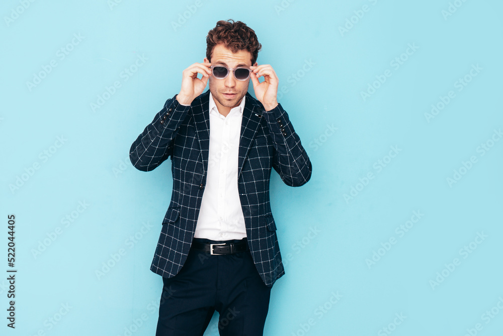 Portrait of handsome confident stylish hipster lambersexual model. Sexy modern man dressed in black elegant suit. Fashion male posing in studio near blue wall Portrait of handsome confident stylish hipster lambersexual model. Sexy modern man dressed in black elegant suit. Fashion male posing in studio near blue wall