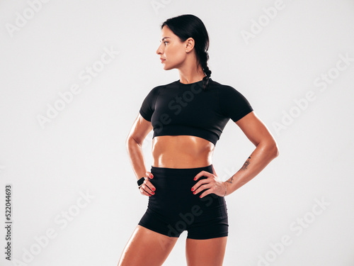 Fitness confident woman in black sports clothing. Sexy young beautiful model with perfect body. Female isolated in studio. Stretching out before training. Posing on grey background © halayalex