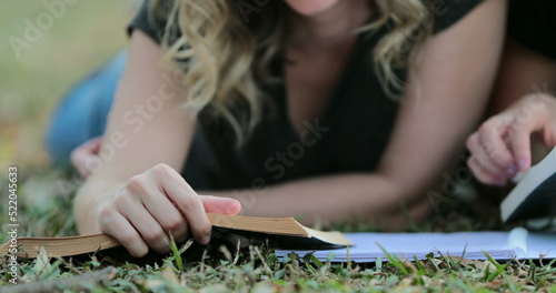 Girl turning page of a book outside lying on grass outdoors. Woman reading book outdoors