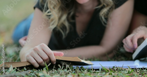 Girl turning page of a book outside lying on grass outdoors. Woman reading book outdoors
