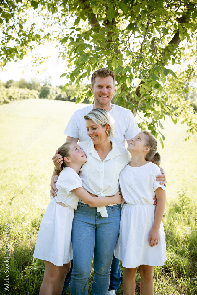 beautiful family with two girls is standing in meadow near walnut tree and has light outfit on and jeans and is happy beautiful family with two girls is standing in meadow near walnut tree and has light outfit on and jeans and is happy