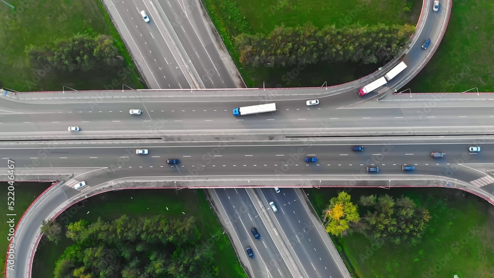 The drone flies over the track during traffic with many interchanges in different directions with a large number of cars that move one after another and change lanes to the desired exit from the track - obrazy, fototapety, plakaty 