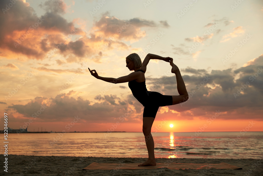fitness, sport, and healthy lifestyle concept - woman doing yoga dancer pose on beach over sunset