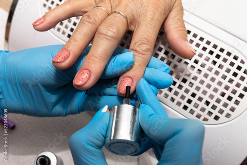 The manicurist applies a topcoat with black dots to the finished hybrid nails with a brush.