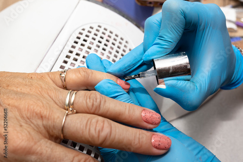 The manicurist applies a topcoat with black dots to the finished hybrid nails with a brush.