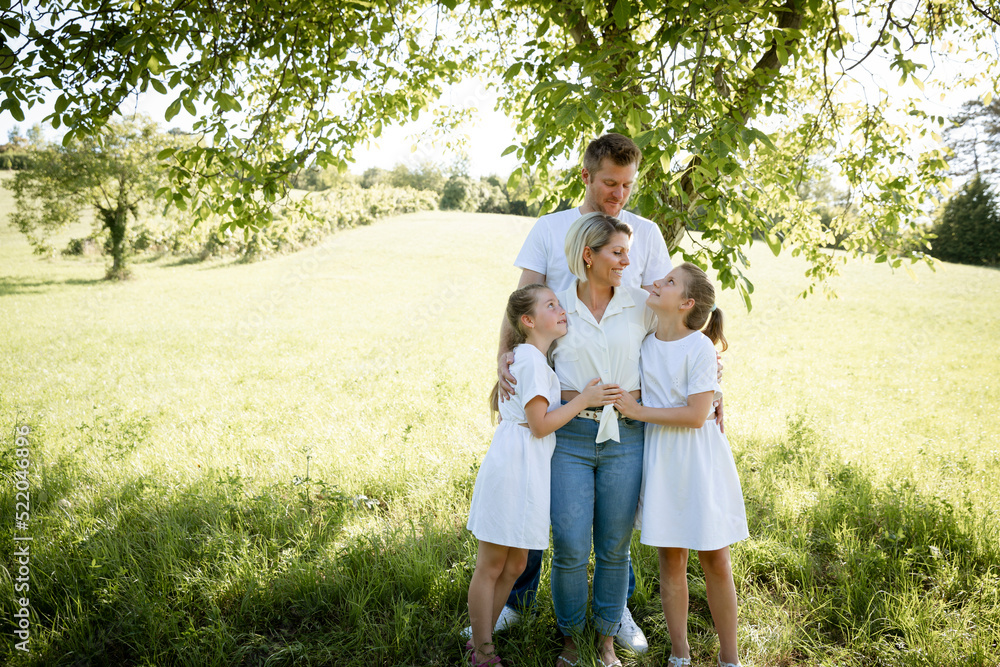 beautiful family with two girls is standing in meadow near walnut tree and has light outfit on and jeans and is happy beautiful family with two girls is standing in meadow near walnut tree and has light outfit on and jeans and is happy