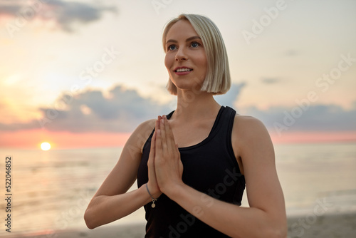 yoga, mindfulness and meditation concept - happy smiling woman meditating on beach over sunset photo