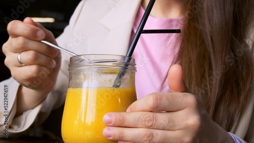 Close-up of a glass cup eating a yellow mango smoothie with a spoon. Consumption of vitamins from fresh fruits to maintain good health and mood. Delicious sweet yellow mango smoothie.