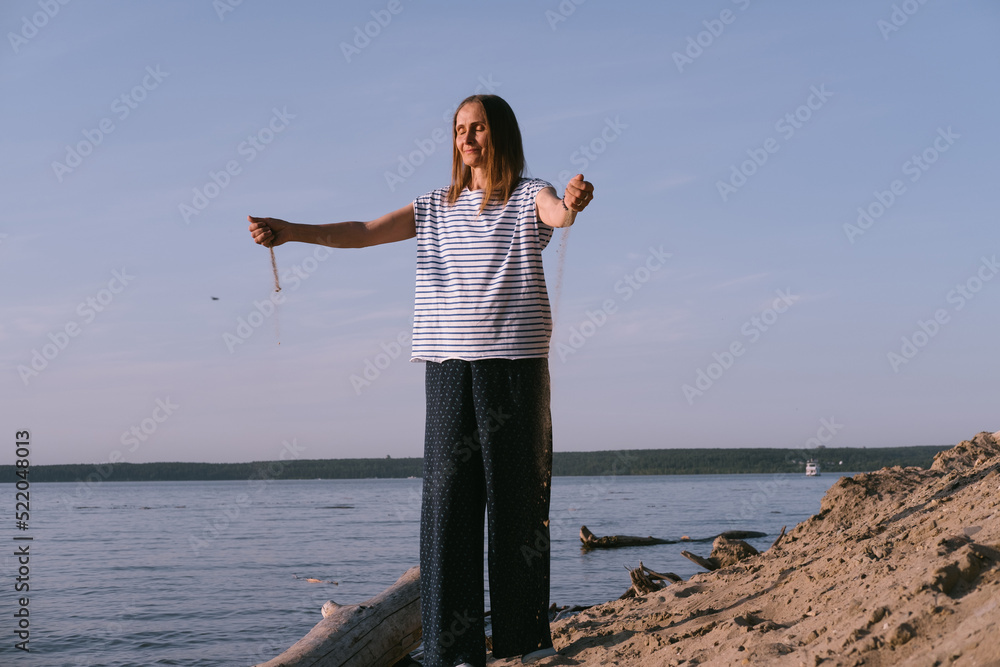 Beautiful female middle age enjoying on sea shore throwing sand with her hands during sunset Beautiful female middle age enjoying on sea shore throwing sand with her hands during sunset
