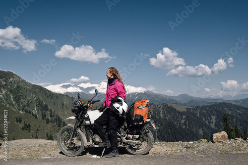 Portrait of beautiful female motorcyclist sitting on motorcycle on top of mountain. Dangerous mountain road in moto trip