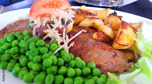 Danish traditional dinner plate with schnitzel, chips and green peas - and a lemon slice with capers, anchovy and horseradish on top photo