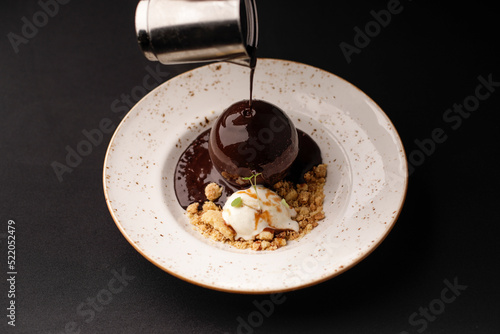 The chef pours hot chocolate on a dessert with icecream