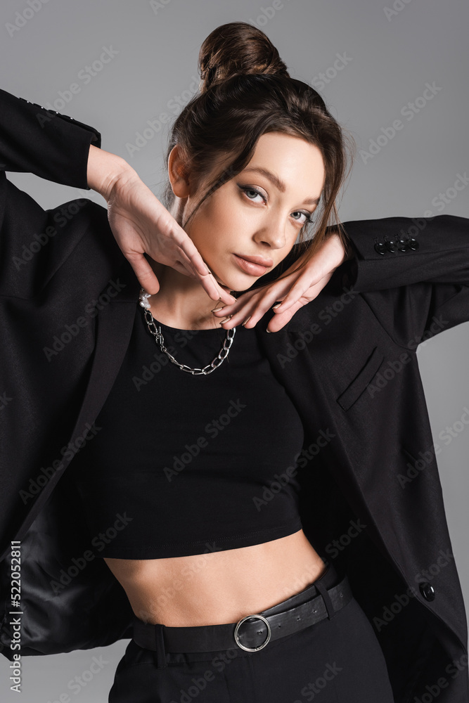 pretty woman in black clothes and silver necklace posing with hands near face isolated on grey pretty woman in black clothes and silver necklace posing with hands near face isolated on grey