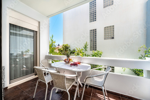 Balcony with furniture, white table served with fruits and wine glasses, four chairs, sunny summer day, holiday concept. 