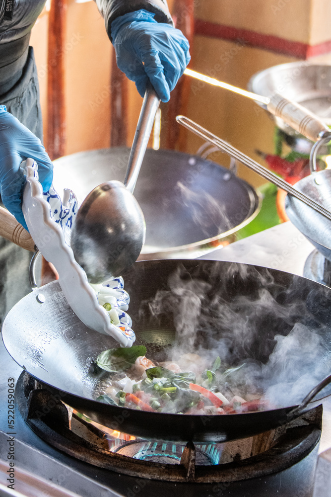 Obraz premium Close-up of fresh Thai cooking in a steaming wok with a big ladle